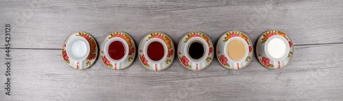 Six cups and saucers on a wooden table filled with water, juice, tea, coffee, milk and coffee with milk