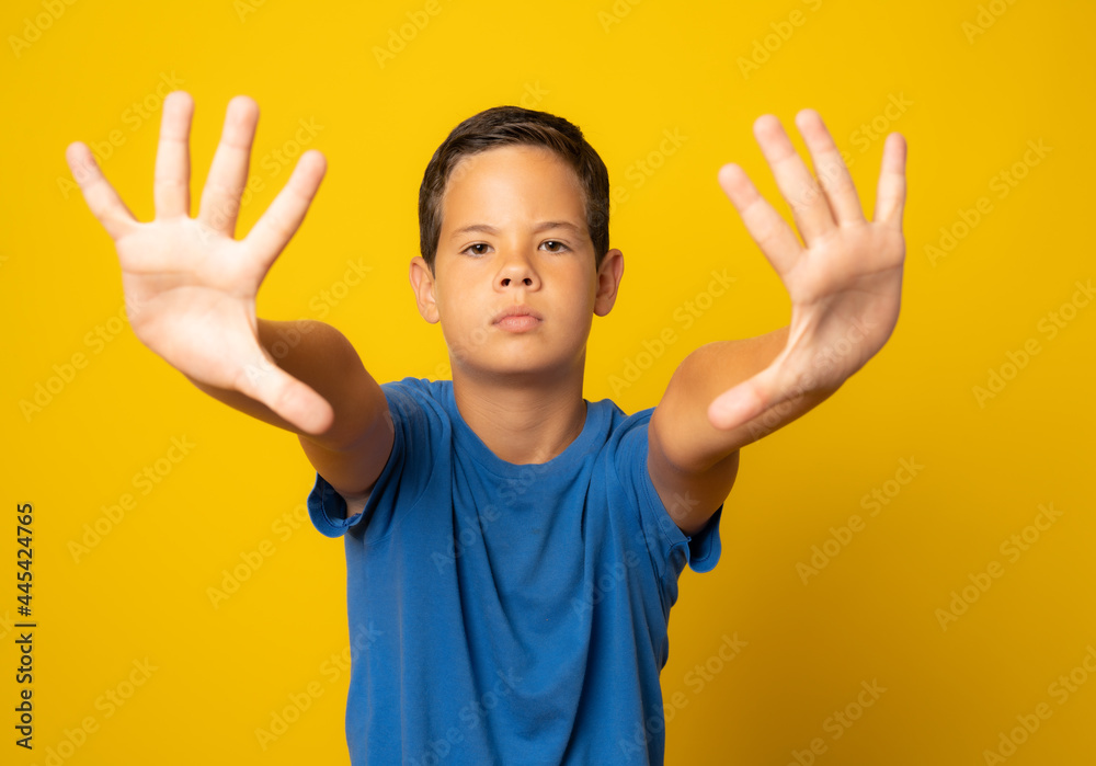 Beautiful kid boy wearing casual t-shirt standing over isolated yellow background doing stop sing with palm of the hand. Warning expression with negative and serious gesture on the face. Beautiful kid boy wearing casual t-shirt standing over isolated yellow background doing stop sing with palm of the hand. Warning expression with negative and serious gesture on the face.