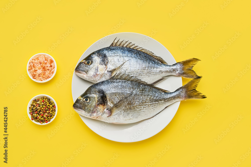 Raw dorado fish with spices on a white plate on a yellow background. Flat lay