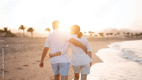 Happy mature senior couple walking and looking at each other on beach during sunset. Aging together and retirement lifestyle concept                                © D'Action Images