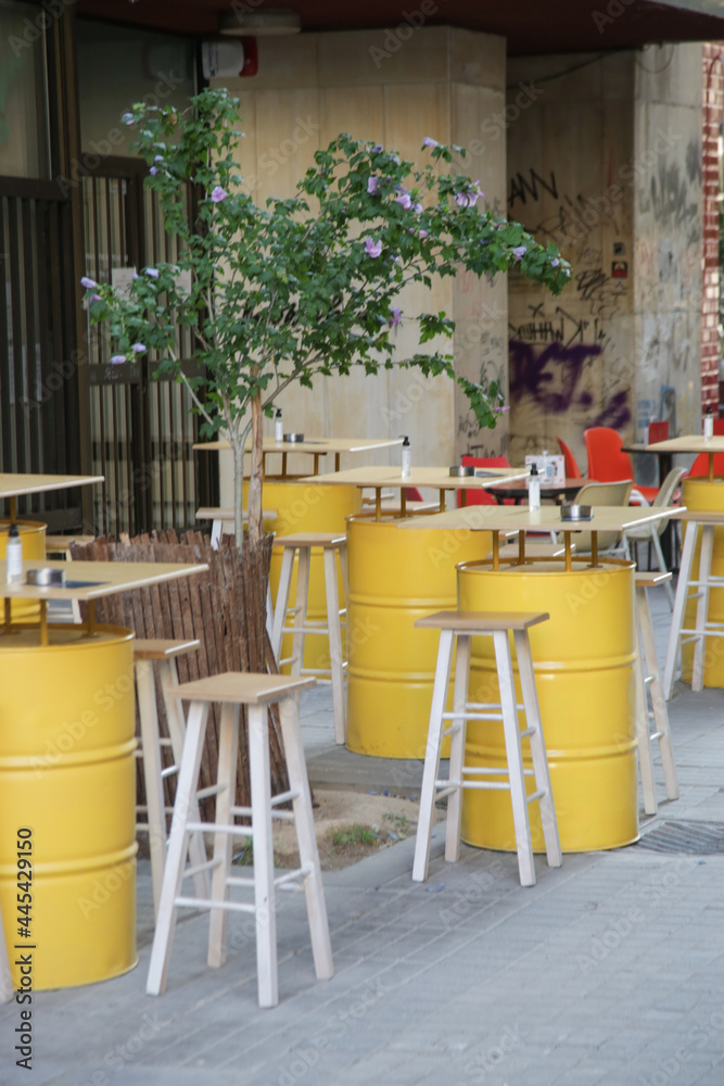 Hipster cafe in the street with yellow barrel tables and chairs, no people