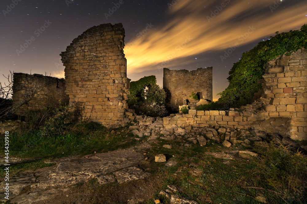 imagen nocturna de una casa de piedra abandonada, con piedras en el suelo, el cielo estrellado y una nube 