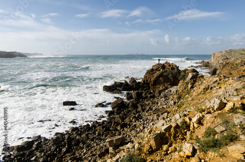 imagen de la costa de Galicia con un pescador en la punta del acantilado con el cielo azul y nubes 