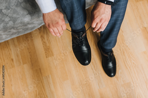 A man, a businessman, ties his shoelaces with his hands on black shiny leather shoes, getting ready for work. Photography, concept, top view.