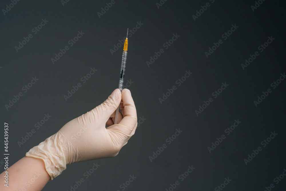 Close-up hands of unrecognizable nurse wearing white latex gloves holding syringe on isolated black background. Studio shot of healthcare worker with protective gloves is holding syringe, closeup. Close-up hands of unrecognizable nurse wearing white latex gloves holding syringe on isolated black background. Studio shot of healthcare worker with protective gloves is holding syringe, closeup.
