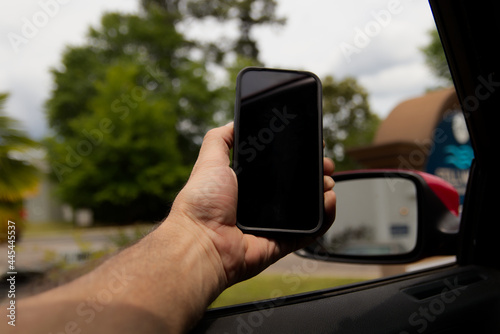 Person holding a cellphone out of a car window