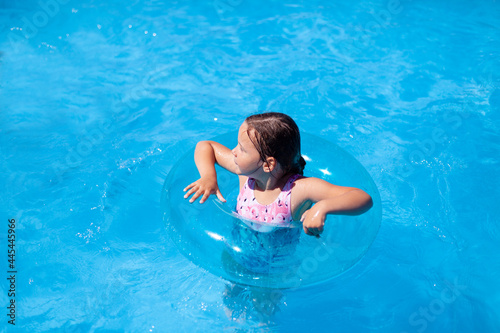 a child learning to swim is held for safety by a blue transparent inflatable circle in the sea, the concept of safe recreation on the water. 