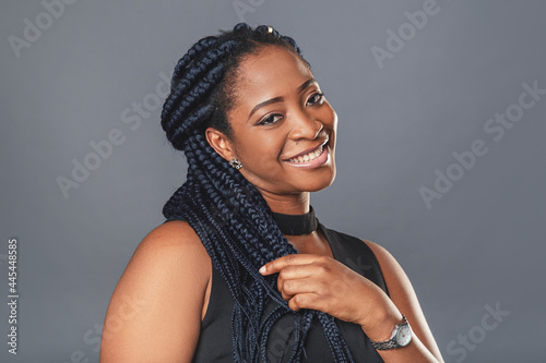 A young dark-skinned woman in a casual atmosphere looks into the camera with copy space curly black hair braided in pigtails. background color gray