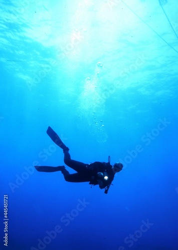 Scuba Diver with a Flashlight Underwater with the Sun Behind