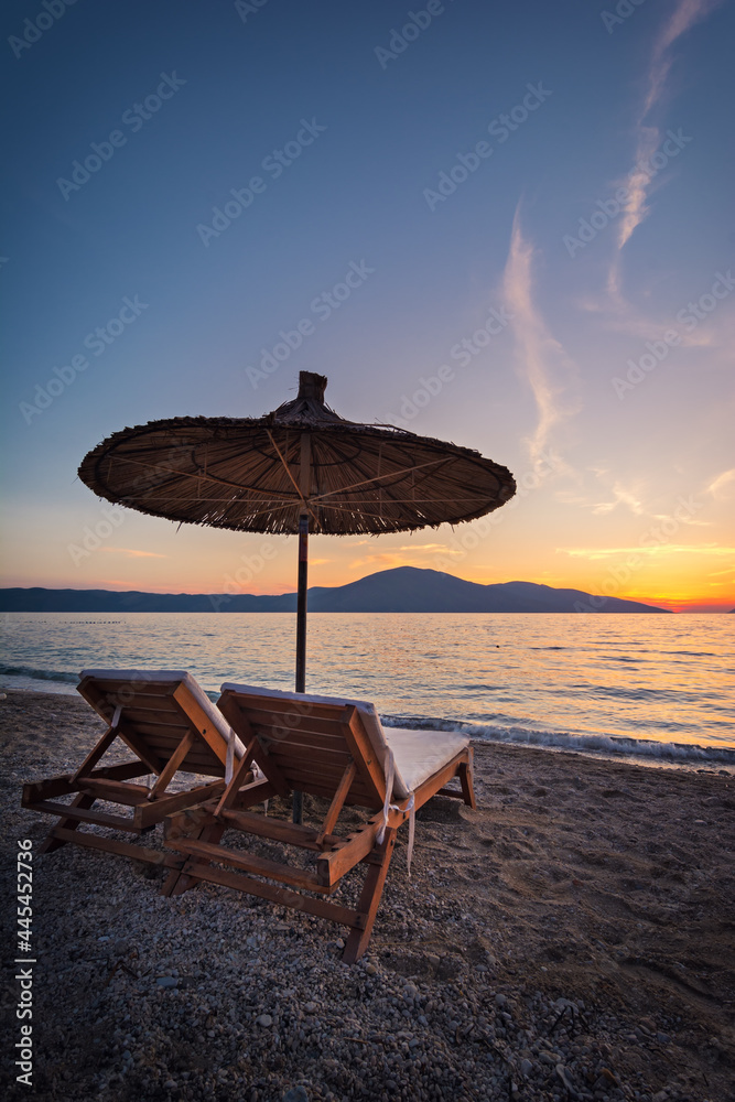 Romantic sunset on the beach with two deck chair under umbrella