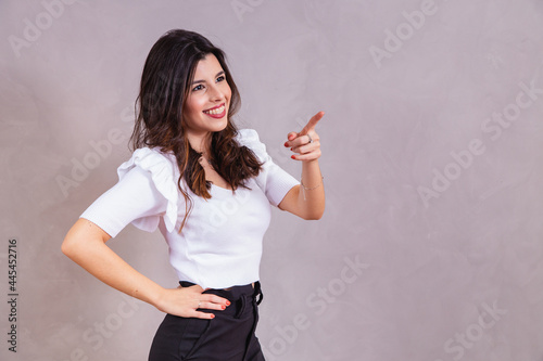 Smiling woman pointing her finger diagonally with free space for text.