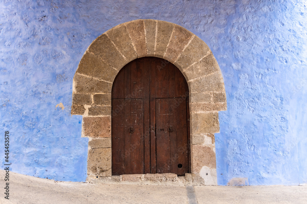 Old and solid wooden door, in a church, with stone portico and blue facade. 