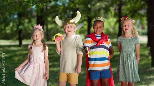 Group of diverse children in costumes looking at camera and screaming joyfully. Boys wearing red cape, king crown and viking helmet, girls in princess diadem and flower headband. Kids role playing