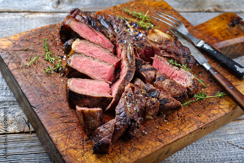 Rustic traditional barbecue dry aged wagyu porterhouse beef steak bistecca alla Fiorentina sliced and served as close-up on a wooden board