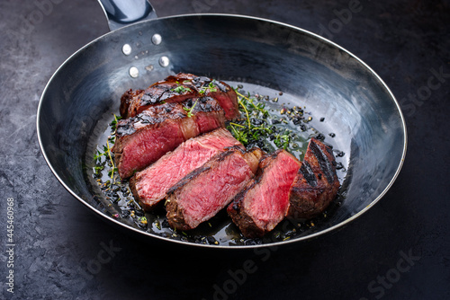 Traditional barbecue dry aged wagyu rib-eye beef steaks with herbs and black salt sliced and served as close-up in a wrought iron skillet on a black board