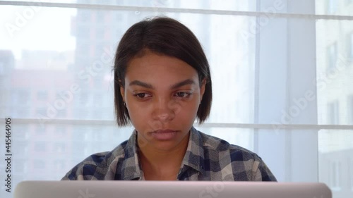 A young black woman sitting at home looking at a laptop monitor. Working and learning online during a pandemic.