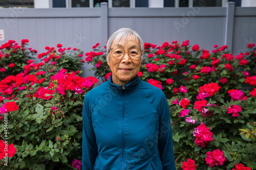 Senior woman wearing eyeglasses standing in front of red flower garden photo