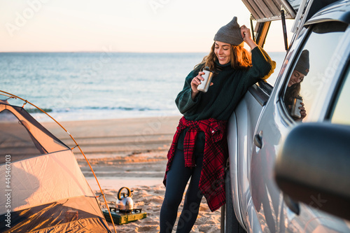 Young woman enjoying coffee in travel mug while beach car camping photo