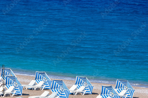 Colorful umbrellas and sunbeds on an empty beach resort - vacation concept on Greece islands in Aegean and Mediterranean seas