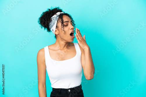 Young latin woman isolated on blue background yawning and covering wide open mouth with hand