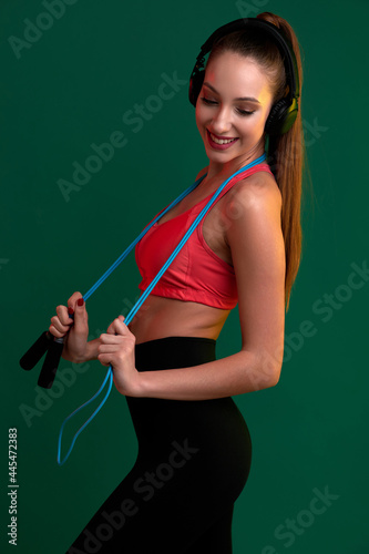 Slender beautiful sporty woman with a skipping rope listening to music in headphones © khmelev