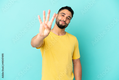 Young arab man isolated on blue background happy and counting four with fingers