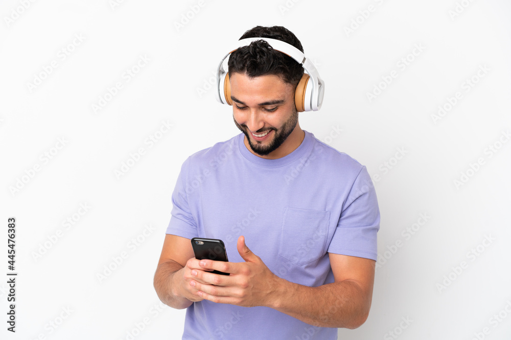 Fototapeta premium Young arab man isolated on white background listening music and looking to mobile