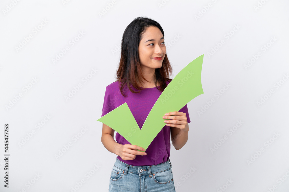 Young Vietnamese woman isolated on white background holding a check icon and looking side Young Vietnamese woman isolated on white background holding a check icon and looking side