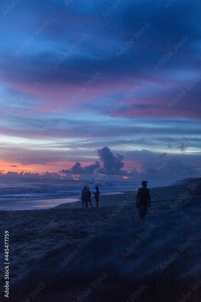 silhouettes of people walking on the beach during their vacations at sunset