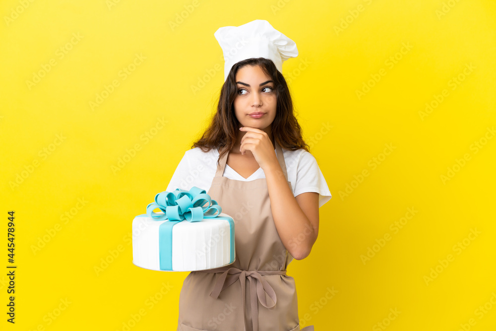 Young caucasian pastry chef woman with a big cake isolated on yellow background having doubts Young caucasian pastry chef woman with a big cake isolated on yellow background having doubts