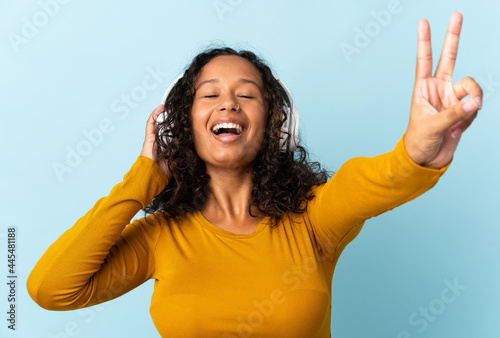 Teenager cuban girl isolated on blue background listening music and singing