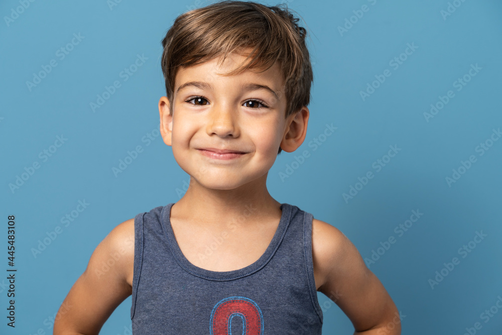 Front view of small caucasian boy four years old standing in front of blue background studio shot child smiling happiness and joy concept Front view of small caucasian boy four years old standing in front of blue background studio shot child smiling happiness and joy concept