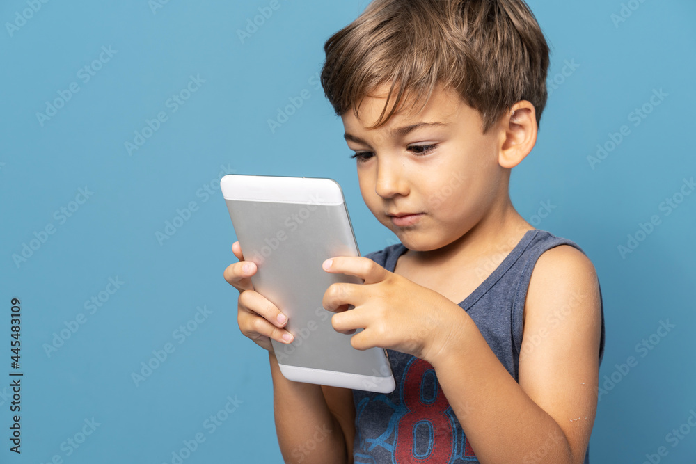 Front view of small caucasian boy four years old standing in front of blue background studio shot standing and using digital tablet Front view of small caucasian boy four years old standing in front of blue background studio shot standing and using digital tablet