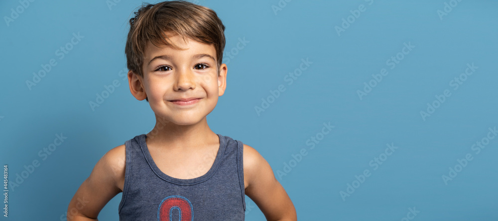 Front view of small caucasian boy four years old standing in front of blue background studio shot child smiling happiness and joy concept Front view of small caucasian boy four years old standing in front of blue background studio shot child smiling happiness and joy concept