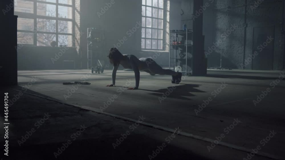 Woman having sport challenge in gym. Female athlete making push ups on floor