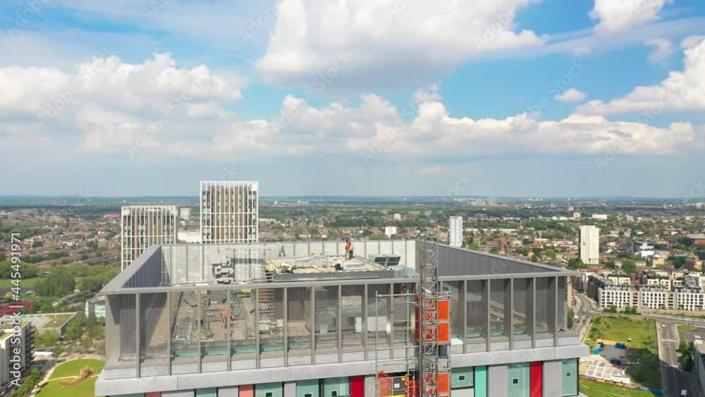 Orbit shot around top of tall building. Construction workers working on roof. Aerial panoramic view of urban neighbourhood Orbit shot around top of tall building. Construction workers working on roof. Aerial panoramic view of urban neighbourhood