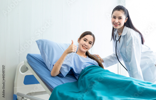 Obraz na płótnie Asian young female patient on bed showing thumbs up with smiley face very good symptom to asian young female nurse doctor in hospital background. w salonie