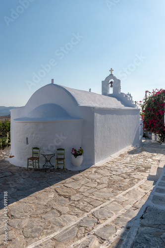Traditional cycladitic alley with a narrow street, a whitewashed church and a blooming bougainvillea in Chora Amorgos Greece