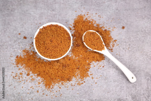 Indian Organic Jaggery Powder on a ceramic white bowl with white spoon - Top View photo