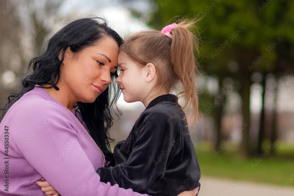 Fototapeta premium lonely sad mother touching with foreheads with daughter, at evening park outdoors.Summer evening,closeup shot.