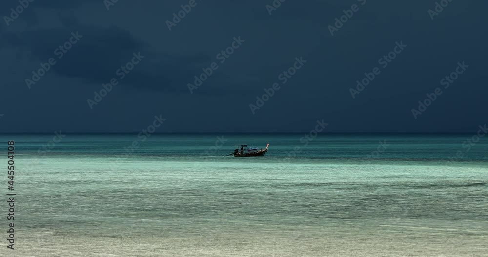 Static shot of dramatic stormy seascape with longtail boat sailing in Andaman sea Thailand. Dark blue cloudy sky covers half the frame, bright glowing turquoise water shines in the foreground