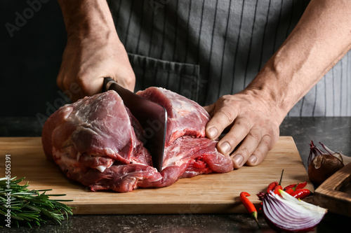 Man cutting raw pork meat on dark background, closeup