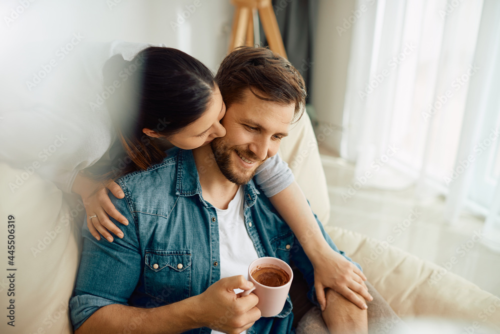 Happy man enjoys in cup of coffee with his wife while she is embracing him at home. Happy man enjoys in cup of coffee with his wife while she is embracing him at home.