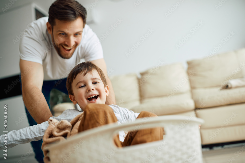 Carefree boy has fun while his father pushes him in a laundry basket at home. Carefree boy has fun while his father pushes him in a laundry basket at home.