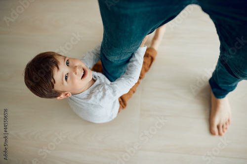 Happy little boy has fun while holding on to his father's leg and looking at camera.