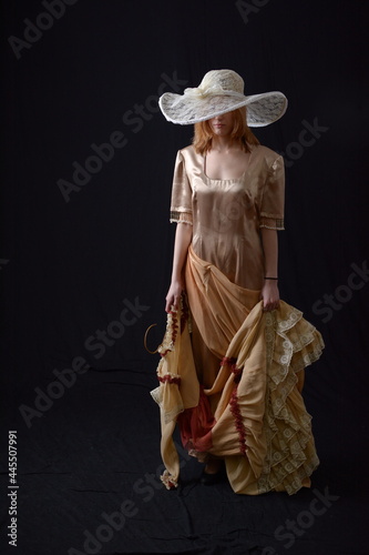 Fényképezés A girl in an old dress and hat stands on a dark background and is sad