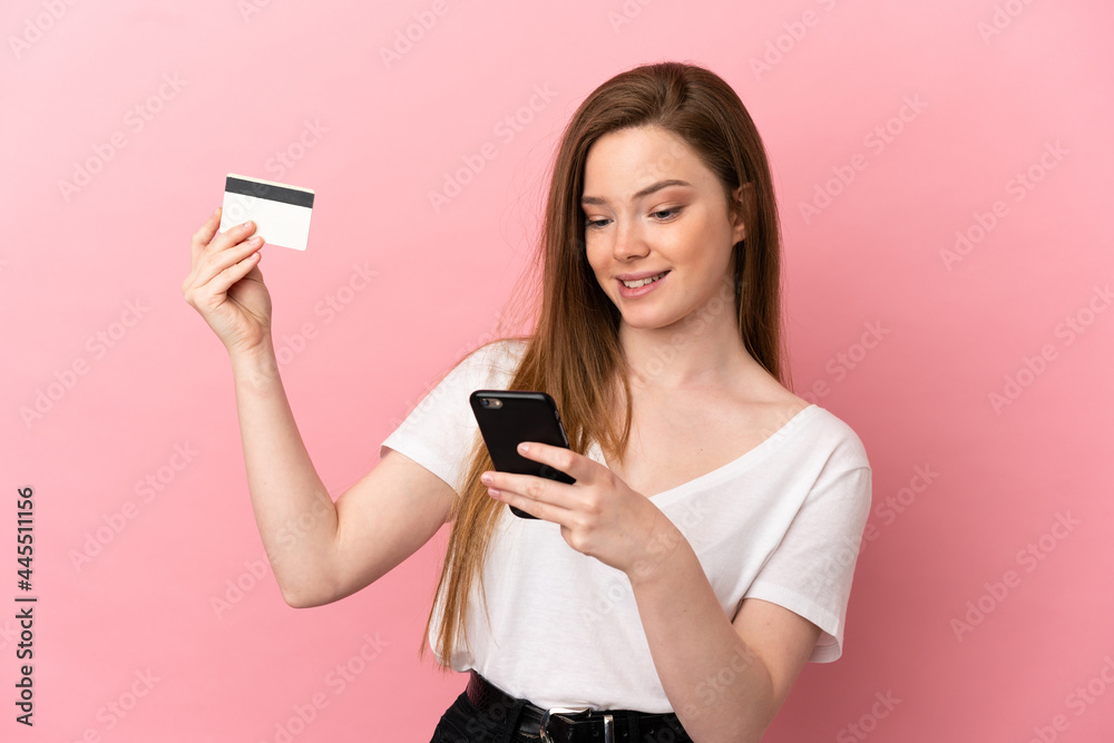 Teenager girl over isolated pink background buying with the mobile with a credit card Teenager girl over isolated pink background buying with the mobile with a credit card