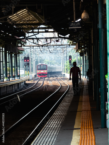 Ttrain in the station, a man walks alone beside the railroad tracks. Jakarta, Indonesia - 16 April 2021 at Gambir station

 photo
