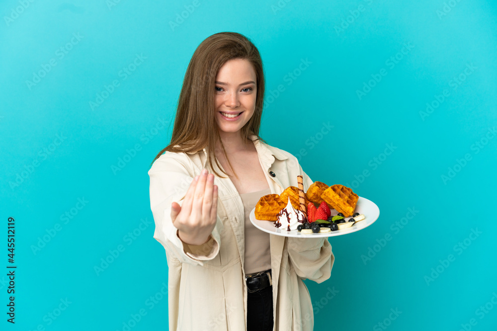 Teenager girl holding waffles over isolated blue background inviting to come with hand. Happy that you came