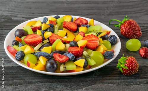 Salad in a white plate made of fresh fruits from grapes, nectarine, kiwi and strawberries, blueberries, honeysuckle on a dark wooden background.Top view, copy of the space Категория Еда 